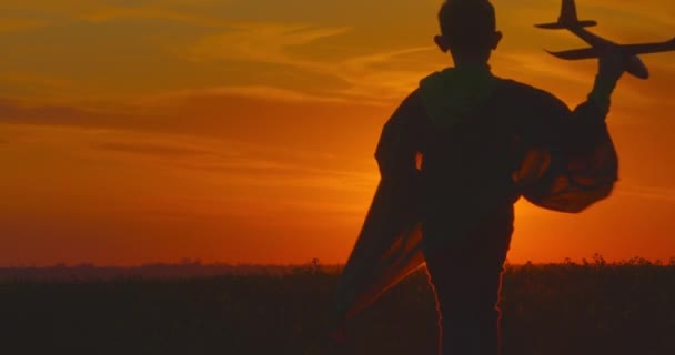 Un niño está corriendo por un campo con un avión en la mano. Puesta de sol. 4K — Vídeo de stock