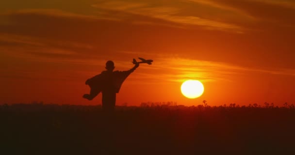 Een jongen rent over een veld met een vliegtuig in zijn hand. Prachtige zonsondergang. 4K — Stockvideo