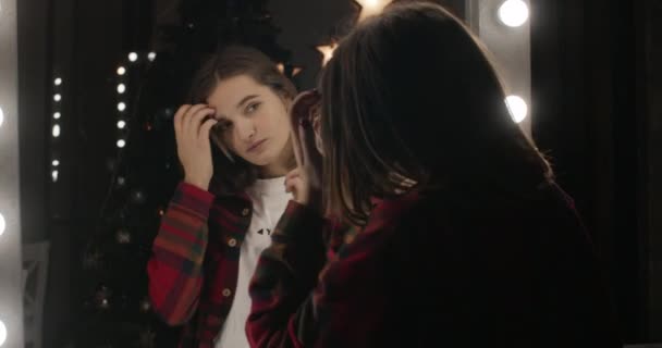 Flickan tittar sig i spegeln och rätar ut håret. 4K — Stockvideo