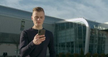 Havaalanının girişinde duran adam telefonda mesajlaşıyor. Merhaba, uçağın gelişini bekliyor. Güneşli bir gün. 4K