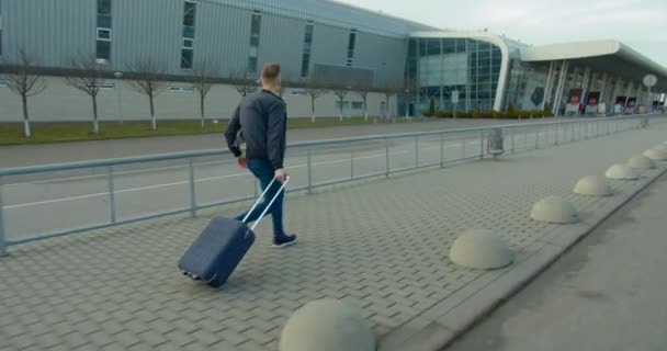 O tipo está a correr para o aeroporto com uma mala. Atrasado para o avião. Dia ensolarado . — Vídeo de Stock