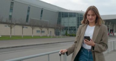 Bavullu kız bir mesaj yazıyor ve bir araç bulmaya gidiyor. Uçakla git. Güneşli bir hava. 4K