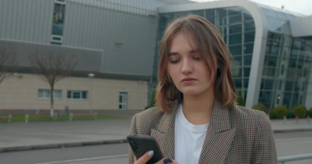 Uma jovem está escrevendo mensagem e sorrindo. O cabelo voa ao vento. Viaje de avião. Tempo ensolarado. 4K — Vídeo de Stock