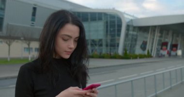 Güzel kız havaalanının yanında dururken gülümsüyor ve telefonda mesaj atıyor. 4K