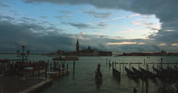 Gondolier arrive au port avec les passagers dans une gondole avec le coucher du soleil et les navires en arrière-plan. Venise, Italie. 4K — Video