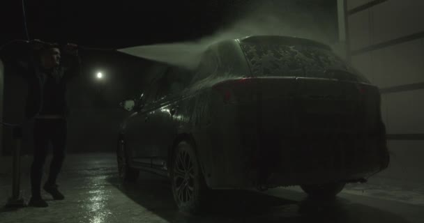En kille spolar skum från en bil vid en självbetjäning biltvätt. 4K — Stockvideo