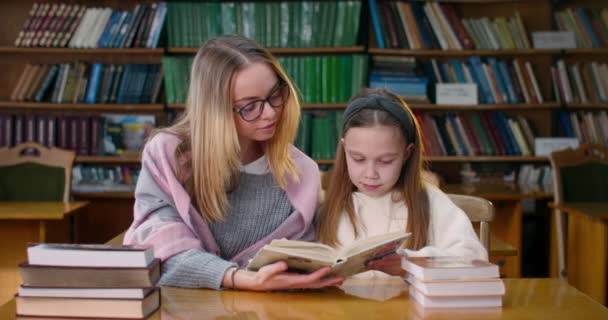 Две девочки читают книгу в читальном зале библиотеки. 4k — стоковое видео