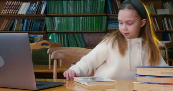 Ένα κοριτσάκι έρχεται στο γραφείο με το βιβλίο και το ανοίγει. Δωμάτιο ανάγνωσης στη βιβλιοθήκη. 4K — Αρχείο Βίντεο