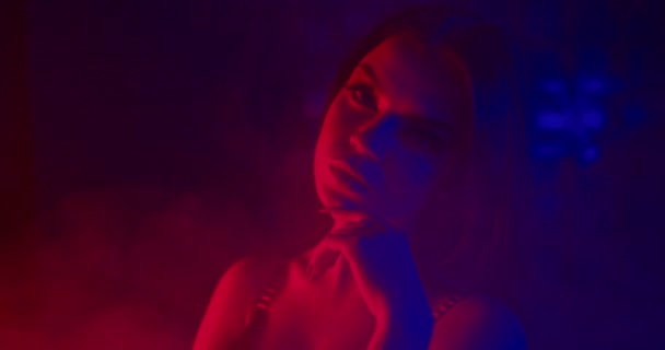 Güzel bir kız cinsel olarak parmağını yüzüne uzatıyor. Mavi ve kırmızı neon ışıklarla çekiliyor. 4k — Stok video