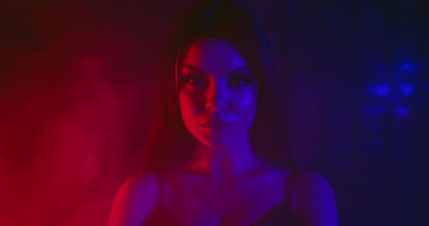 Sexig tjej tittar på kameran. Skjuta på en blå och röd neon bakgrund med rök. 4k — Stockvideo