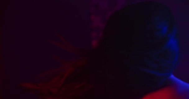 Una bella ragazza sta girando e i suoi capelli volano nel vento. Sparatoria con luci al neon blu e rosse. 4K — Video Stock