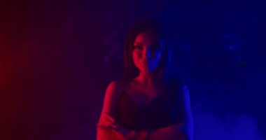 Güzel bir kız poz veriyor ve kameraya bakıyor ve cinsel olarak elini yüzüne kaldırıyor. Mavi ve kırmızı neon ışıklarla ateş ediyorlar. 4k