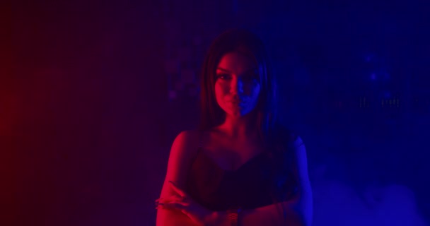 Ein schönes Mädchen posiert und blickt in die Kamera und hebt sexuell ihre Hand zu ihrem Gesicht. Schießen in blauem und rotem Neonlicht. 4k — Stockvideo