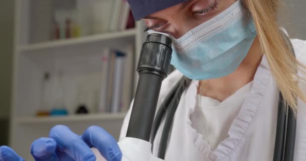 Un employé de laboratoire examine un microscope et change de lentille. Expériences en laboratoire. Cherchez un vaccin. 4K — Video