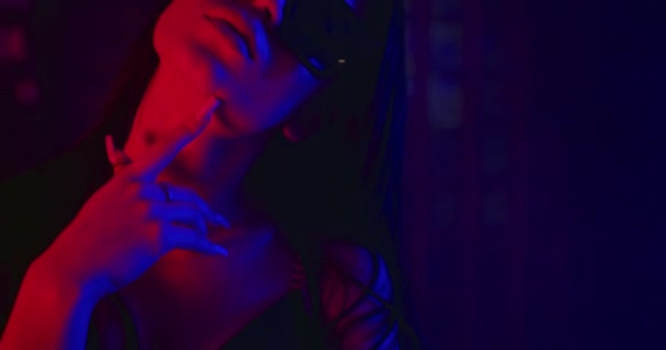 Közelkép egy lányról, aki szexuálisan végigsimítja az ujját a nyakán. A divat szemüvegben néz ki. Kék és piros neon. 4k — Stock videók