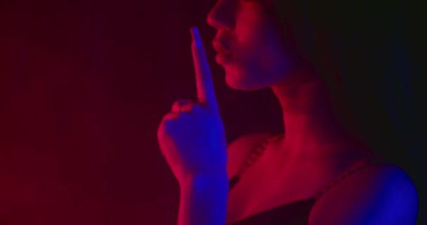 Una hermosa chica sexy está poniendo su dedo en sus labios y bajándolo. Disparando en luces de neón azules y rojas. Disparos de cerca desde un lado. 4k — Vídeo de stock