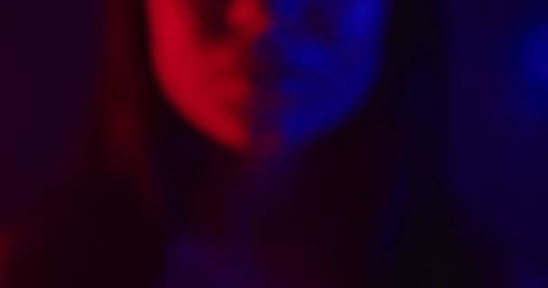 Uma linda garota está de pé em luz de néon azul e vermelho e sexualmente coloca o dedo nos lábios. Tiroteio de perto. 4K — Vídeo de Stock