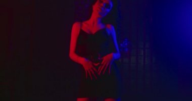 Kız ellerini belinden geçirip göğsüne doğru kaldırıyor ve saçları rüzgarda uçuşuyor. Moda bakışı. Mavi-kırmızı neon. 4k