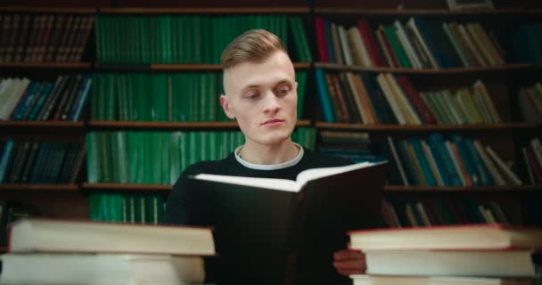 Hij probeert de nodige informatie te vinden door in het boek te kijken. Onderwijs in de bibliotheek. 4K — Stockvideo