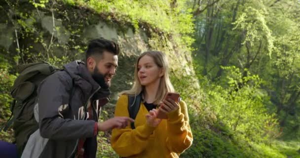 A guy and a girl are looking at a map on their smartphone. Hiking in the forest. 4k — Stock Video