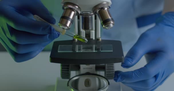 Strzelanina z bliska. Pracownik medyczny nakłada substancję testową na szkiełko mikroskopu. Eksperymenty w laboratorium. Szukajcie szczepionki. 4K — Wideo stockowe