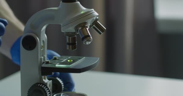 Prise de vue rapprochée. Un employé de laboratoire examine un microscope et l'ajuste. Expériences en laboratoire. Cherchez un vaccin. 4K — Video