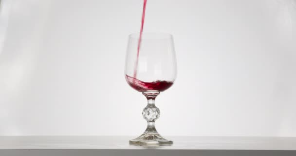 Nahaufnahme. Der Rotwein ergießt sich in ein Glas. Weißer Hintergrund. 4K — Stockvideo