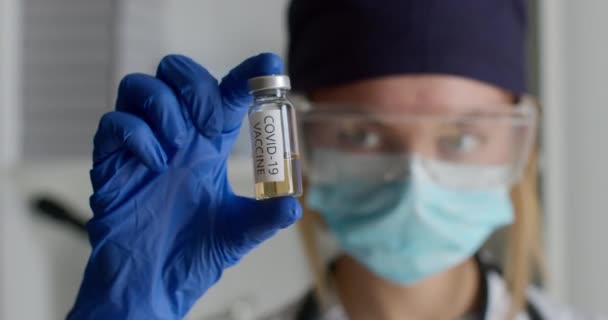 Un primo piano. Un operaio di laboratorio in tuta protettiva mostra una provetta con il vaccino COVID-19. Esperimenti in laboratorio. 4K — Video Stock