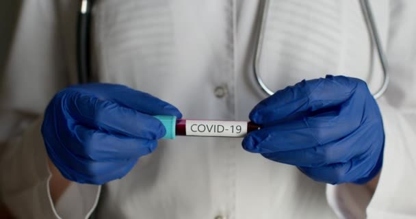 Gros plan. Un travailleur de laboratoire en combinaison de protection montre une éprouvette avec le COVID-19. Expériences en laboratoire. 4K — Video