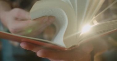 Yakın plan, eller eski bir kitabı çeviriyor ve toz bulutu ışığa doğru uçuyor. 4K