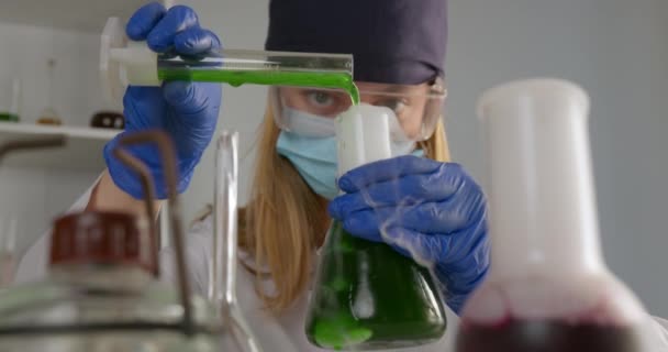 Un trabajador de laboratorio está mezclando componentes en un matraz y observando su reacción. En un frasco frontal con reacciones químicas. Experimentos en el laboratorio. 4K — Vídeo de stock