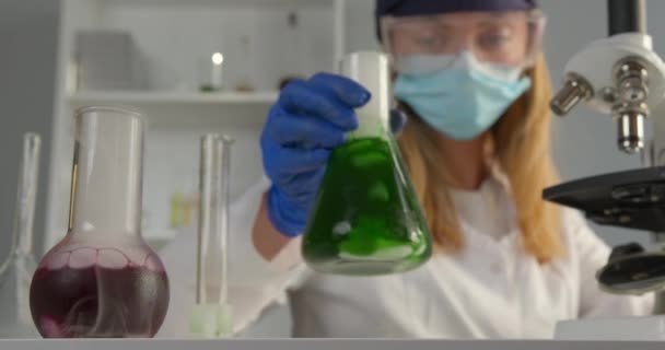 Um trabalhador de laboratório está misturando componentes em um frasco e observando sua reação. Em um microscópio de plano frontal e frasco com reações químicas. Experiências no laboratório. 4K — Vídeo de Stock