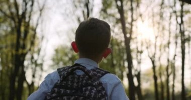 Yakın plan çekim. Bir çocuk sırt çantasıyla parkta yürüyor. Arkadan ateş ediyorlar. 4k