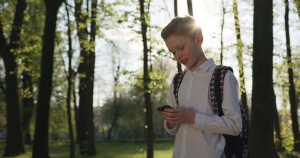 Ein Junge läuft mit Rucksack und SMS durch den Park. 4K — Stockvideo