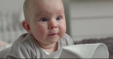 Yakın plan çekim. Bebek yatağın üzerinde yatıyor ve annesinin ne yaptığına bakıyor. 4k