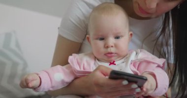 Yakın plan çekim. Anne bebekle oturuyor ve telefonda mesajlaşıyordu. 4K
