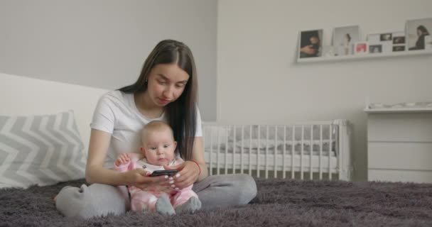 De moeder zit met de baby te sms 'en aan de telefoon. 4K — Stockvideo