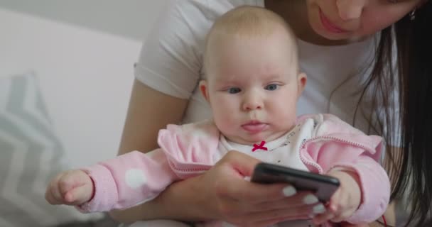 근접 촬영. 어머니는 아기와 앉아서 전화로 문자를 하고 있습니다. 4K — 비디오