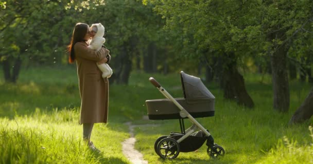 A mãe está segurando o bebê nos braços e beijando-o. Caminhando em Spring Park. 4K — Vídeo de Stock