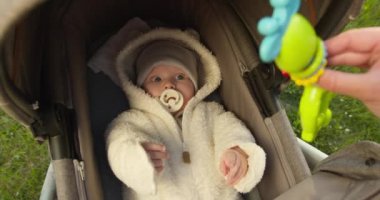 Yakın plan çekim. Bebek bir bebek arabasında yatıyor. Annem bebeği bir oyuncakla sakinleştiriyor. 4K