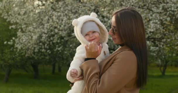 Közelről lőtték le. Anya simogatja a babák orrát és mosolyog. Egy anya egy gyermeket tart a karjaiban. 4K — Stock videók