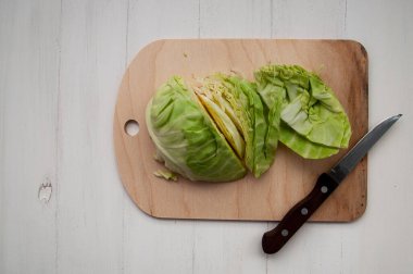 Tahta kesim tahtasına kesilmiş yeşil lahana, tahta saplı bıçak, beyaz ahşap arka planda. Üst görünüm, yatay görüntü.