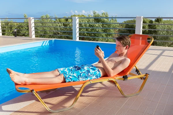 Dutch boy on sunlounger  operating mobile phone at pool — Stock Photo, Image