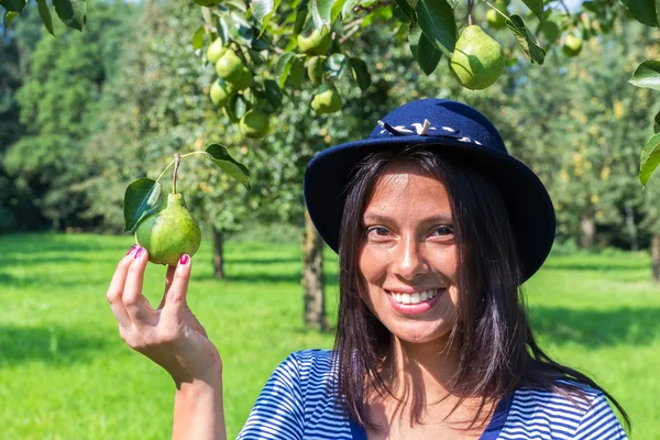 Donna che indossa cappello tenendo pera nel frutteto — Foto Stock