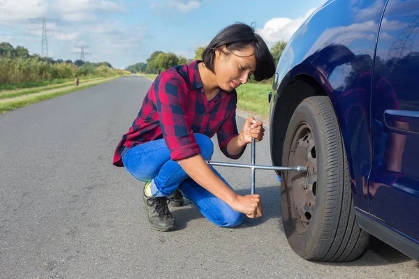 国の道路で車のホイールを変更する若い女性 — ストック写真