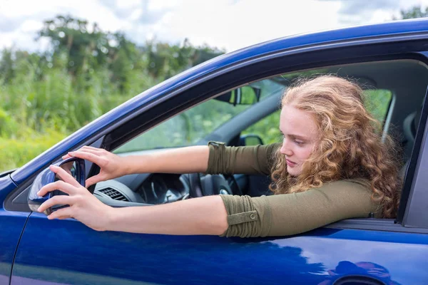 Mujer caucásica ajustando espejo lateral del coche — Foto de Stock