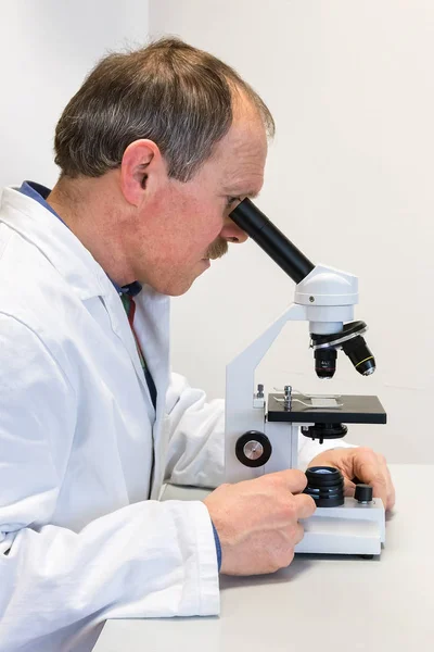 Биолог в лабораторном халате смотрит в микроскоп — стоковое фото