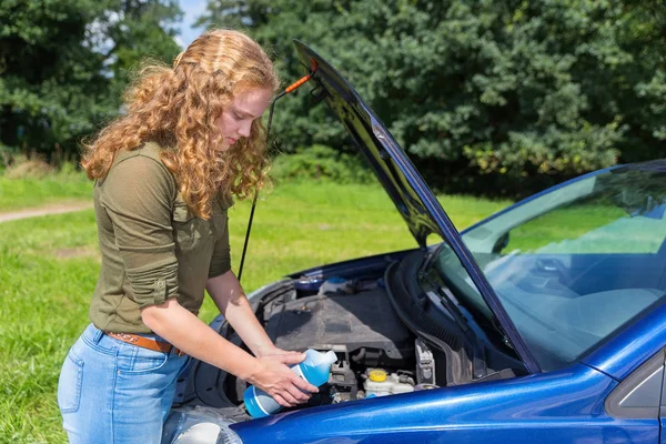 Chica holandesa llenando depósito de coche con líquido en botella —  Fotos de Stock