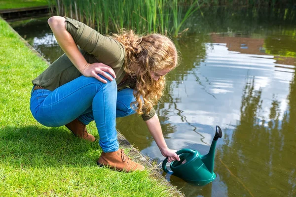 Молодая голландка, наполняющая зеленую кастрюлю водой — стоковое фото