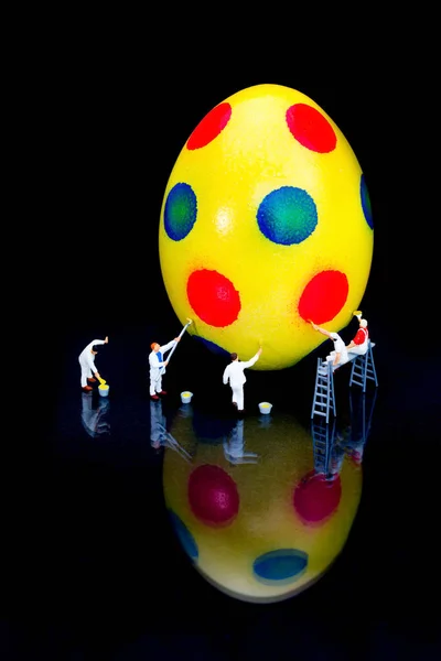Miniature figurines painting yellow easter egg on black